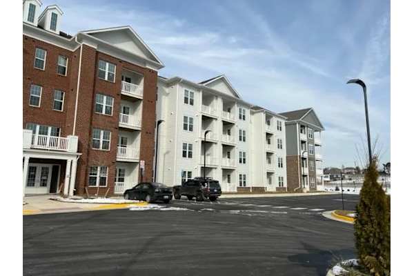 A black car is parked in a parking lot in front of a white and brown building.
